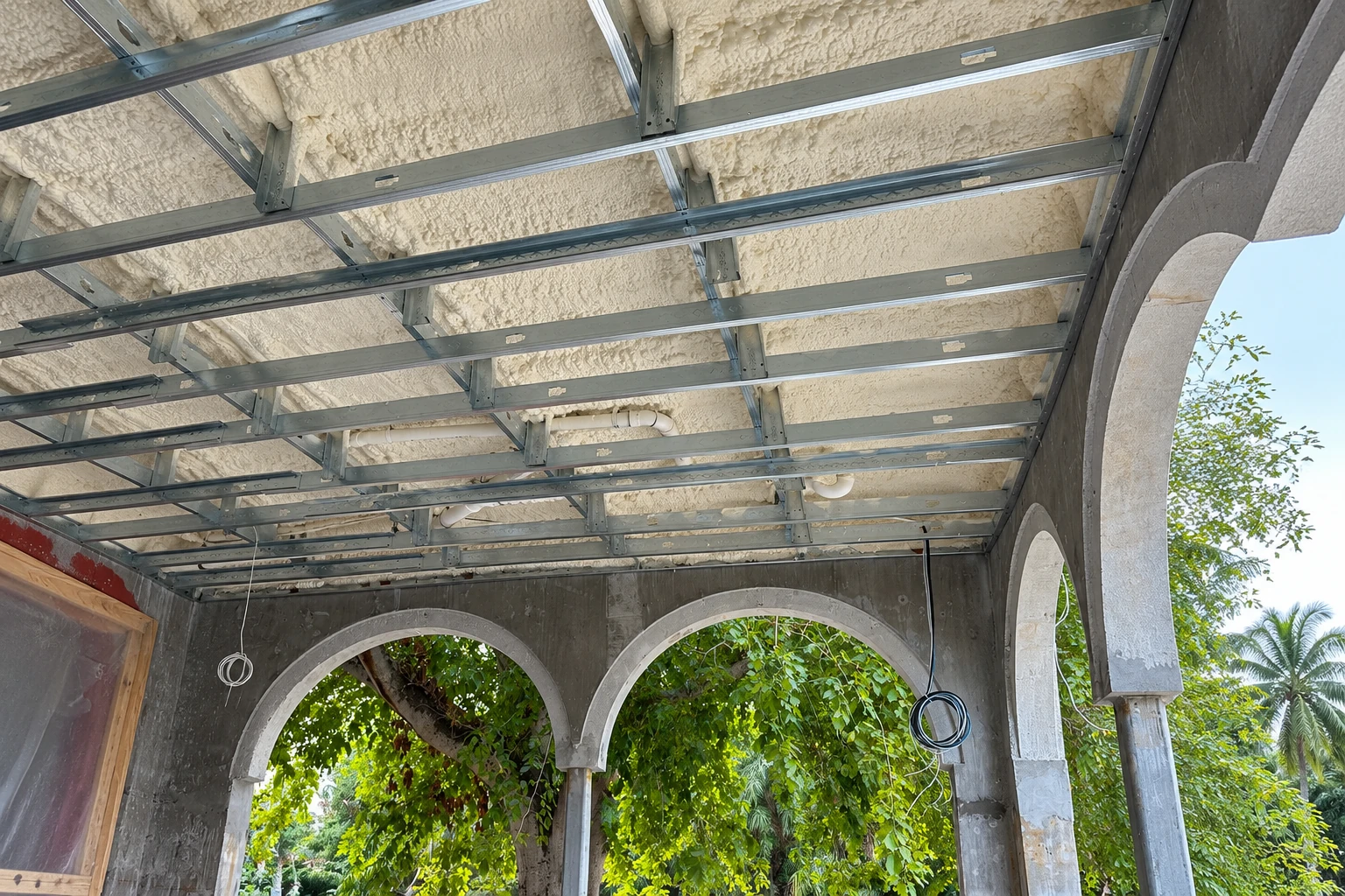 Closed-cell spray foam insulation coats the ceiling above a metal framing grid in an unfinished arched concrete structure.