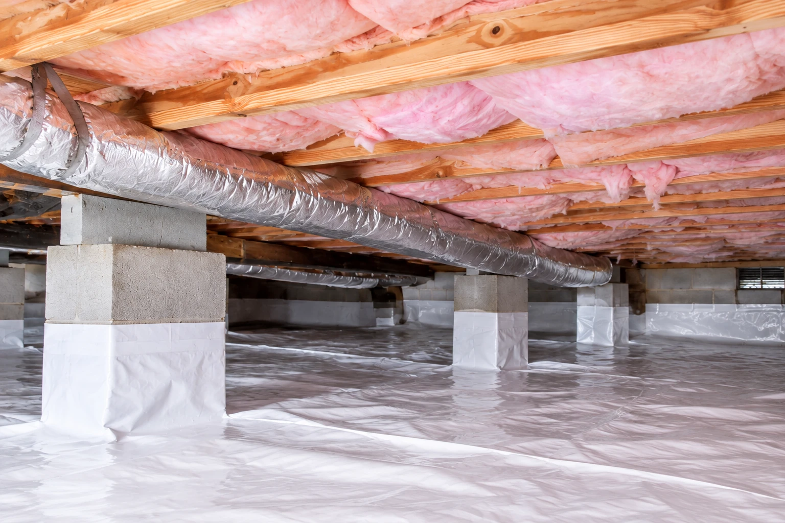 Crawl space with plastic vapor barrier covering the floor and support piers, pink insulation between the floor joists, and silver ductwork.